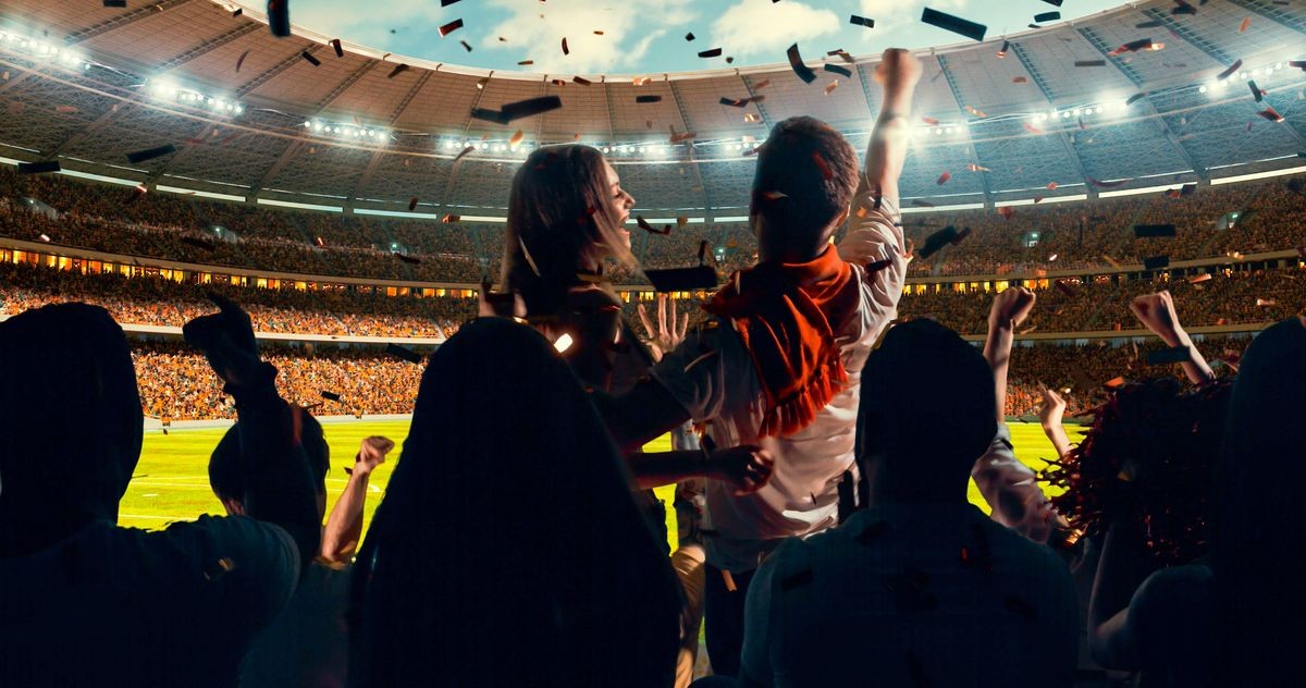 Group of cheering fans watch a sport championship on stadium. Their team wins and everybody are celebrating this event. People are dressed in casual cloth.